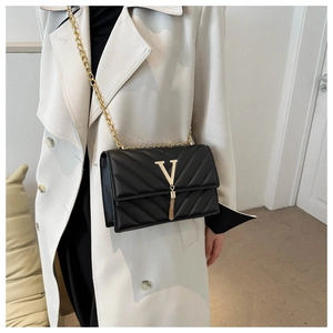 Détail d'un sac à bandoulière noir matelassé avec logo V doré et breloque à franges