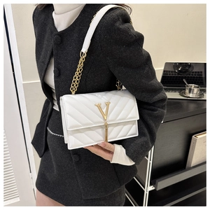 Détail d'un sac à rabat blanc matelassé avec boucle en V dorée et bandoulière chaîne