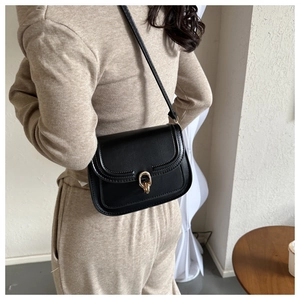 Sac bandoulière classique en cuir noir avec boucle dorée sur une tenue en maille beige