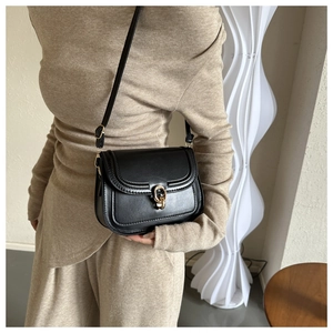 Sacoche selle en cuir noir avec boucle fer à cheval dorée portée à l'épaule sur mannequin