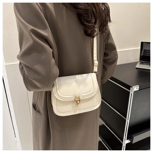 Détail d'un sac bandoulière chic en cuir crème avec fermoir en anneau doré sur manteau