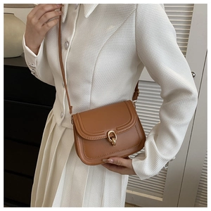 Détail d'un sac besace marron en cuir avec boucle dorée ronde et coutures apparentes
