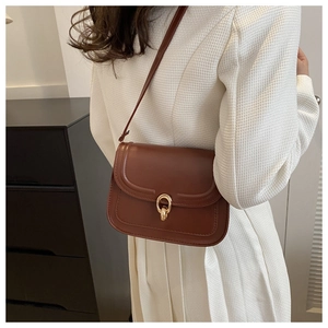 Détail du sac bandoulière en cuir marron foncé avec boucle dorée sur un modèle