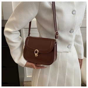 Sac bandoulière en cuir marron avec fermoir doré porté avec un blazer blanc texturé chic