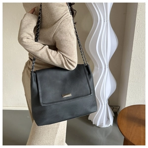 Détail d'un grand sac à bandoulière noir avec rabat, chaîne en métal et texture cuir