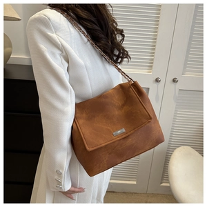 Détail du sac bandoulière en daim caramel avec bandoulière en chaîne et plaque en métal