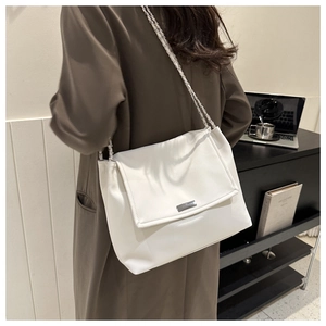 Détail du sac cabas en cuir blanc avec chaîne argentée et logo sur le rabat avant