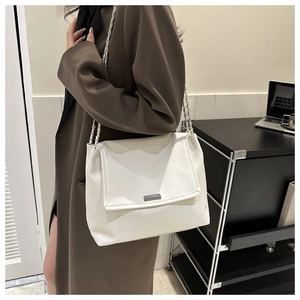 Détail d'un sac à bandoulière en cuir blanc avec chaîne argentée et plaque en métal poli