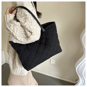 Detail of a large black quilted tote bag with smooth leather straps for women