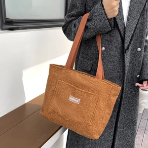 Brown fuzzy tote bag with orange straps and fashion label in a minimalist room