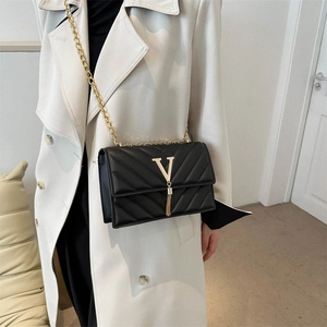 Sac bandoulière noir matelassé avec logo V et chaîne dorée sur un trench-coat beige