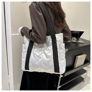Detail of white quilted tote bag with metallic finish and wide black shoulder strap