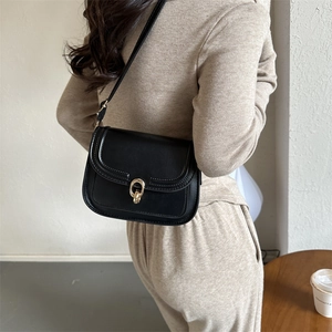 Petit sac carré en cuir noir avec boucle dorée porté par un mannequin élégant
