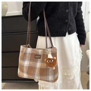 Primer plano de bolso tote de lana a cuadros marrones con asas de cuero y peluche