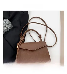 Detail view of brown textured leather handbag with knotted handles and cross-body strap
