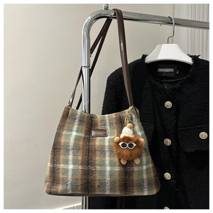 Detalle del bolso tote de felpa a cuadros con correa marrón y colgante de monstruo