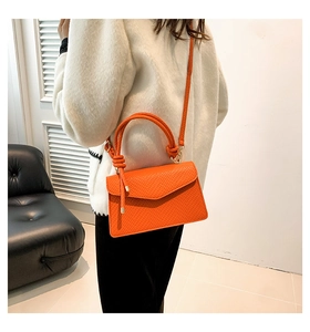 Detailed view of an orange textured leather crossbody bag with a knot handle design