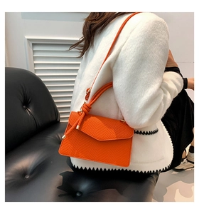 Detail of bright orange embossed leather shoulder bag with gold hardware and knot handle
