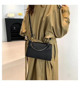 Close-up of black woven texture crossbody bag with gold hardware on khaki coat