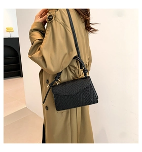 Detail of black embossed leather crossbody bag with golden ring hardware on trench coat