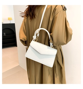 Detailed side view of textured white crossbody bag with gold buckle on trench coat