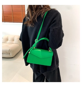 Detail of a bright green crossbody bag with lychee texture and gold metal hardware