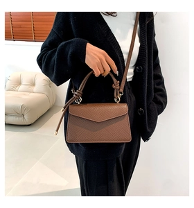 Close-up of brown litchi pattern leather bag with woven knot handle and gold hardware