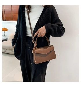 Brown textured leather crossbody bag detail with knotted handle and gold hardware on model