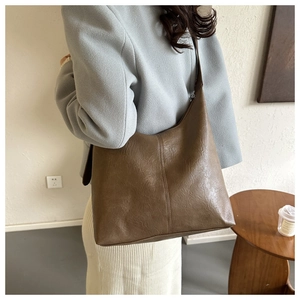 Detail of dark brown PU leather shoulder bag with vertical stitching on model's coat