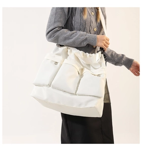 Detail of white nylon tote bag featuring three front cargo pockets with silver buckles