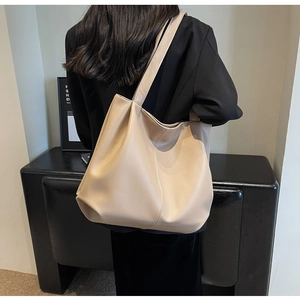 Detailed back view of a large beige tote bag with litchi grain texture on a female model