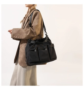 Detail of black nylon crossbody bag with three front utility pockets and silver ring zippers