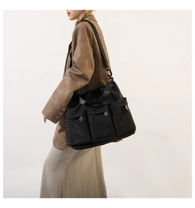 Close-up of black nylon shoulder bag featuring multi-pocket design and silver metal eyelets