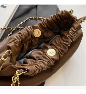 Detail of dark brown pleated leather bucket bag with magnetic gold clasp and chain