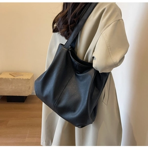 Detail of black pebbled leather tote bag showing large capacity on model in beige coat