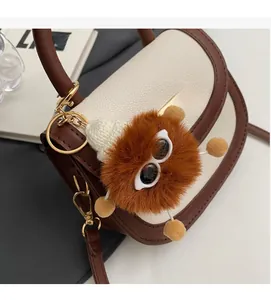 Détail d'un sac bandoulière bicolore en cuir grainé avec un pendentif monstre en peluche