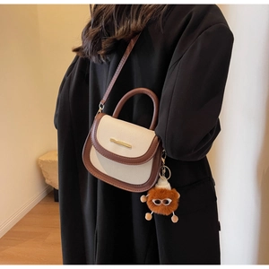 Détail du sac de selle crème et marron avec boucle en métal et breloque sur un manteau noir
