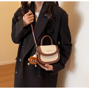 Détail du sac selle bicolore avec barre métallique et breloque en peluche douce