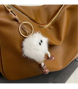 Close-up of fluffy white plush doll keychain with small brown boots on a leather bag