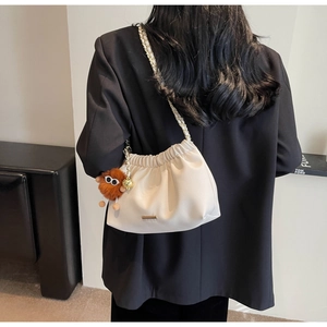 Close-up of white quilted bucket bag with chain strap and cute brown plush monster charm
