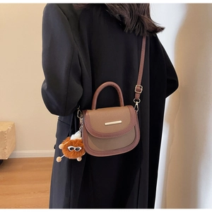 Détail d'un sac selle marron avec un pendentif œil en peluche et ferrures dorées