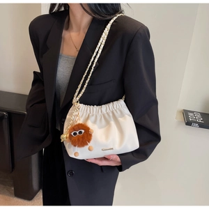 Detail of white drawstring bucket bag with gold chain strap and fuzzy monster charm