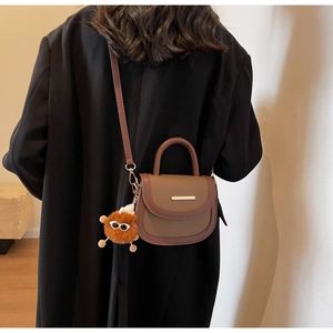 Détail du sac à selle minimaliste avec breloque orange sur un mannequin en manteau noir