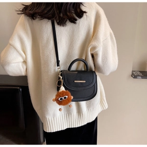 Détail du sac selle en cuir grainé noir avec garniture dorée et breloque monstre en peluche