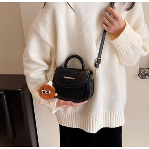 Détail d'un sac selle en cuir grainé noir avec charme en peluche et bandoulière sur modèle