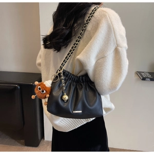 Detail of black pebbled leather bucket bag with gold chain and plush eye pendant