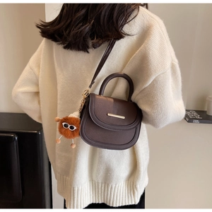 Détail du sac à main marron foncé texture litchi sur modèle avec breloque peluche