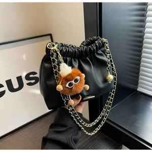 Detail of black pleated cloud bag with gold chain strap and cute plush monster charm