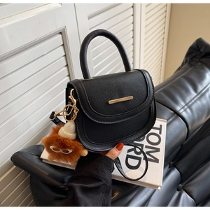 Détail du sac selle en cuir grainé noir avec boucle dorée et breloque en peluche