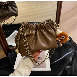 Detail of dark brown pleated cloud bag with golden chain and plush monster charm